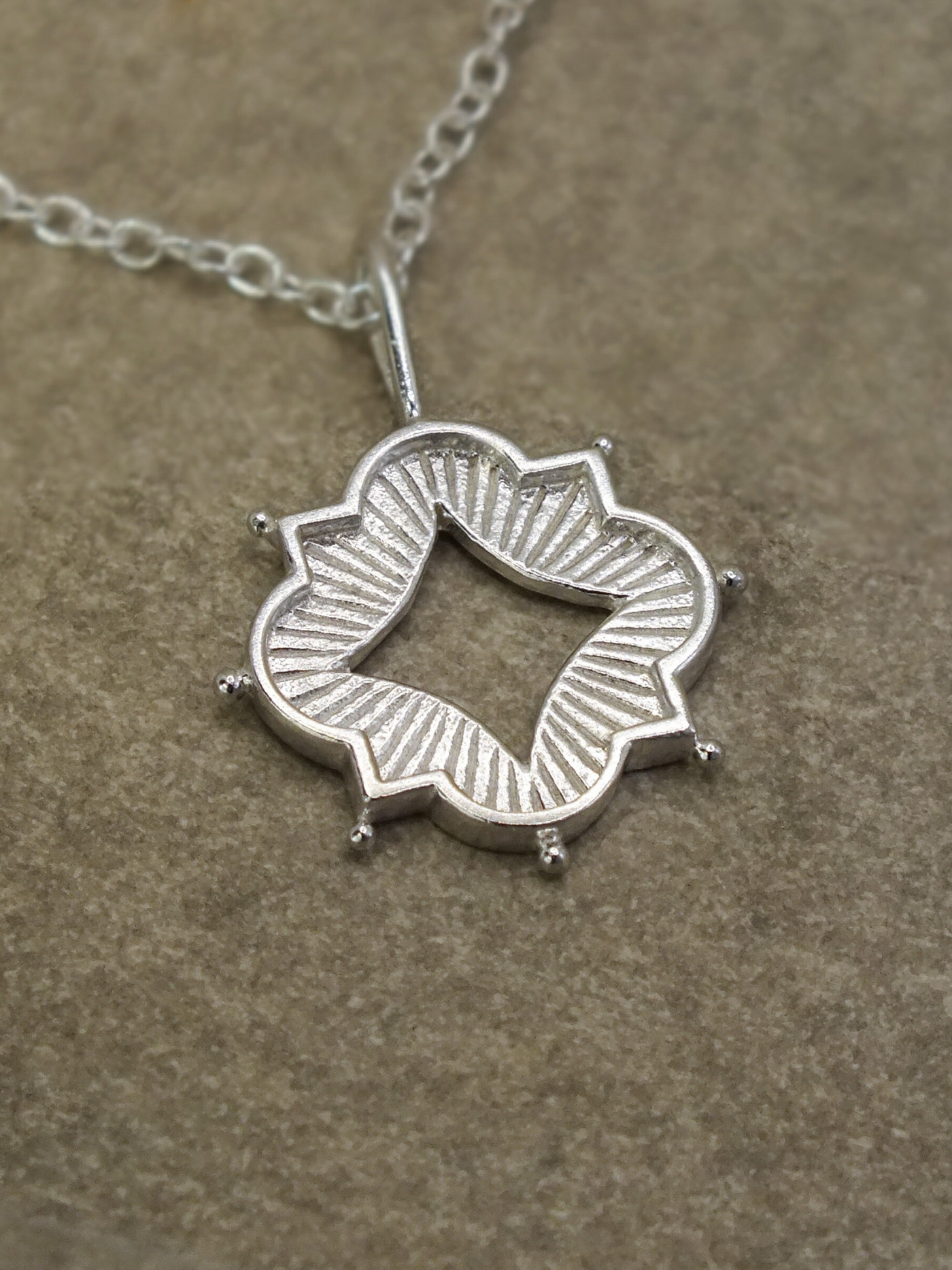 Sterling silver quatrefoil pendant necklace with a central diamond-shaped cutout, inspired by Gothic architecture and sacred geometry, featuring engraved sunburst rays and protective talisman-style detailing with spherical accents, hanging from a delicate silver chain.