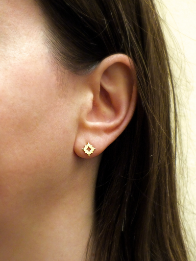 Dainty solid 18k gold stud earrings inspired by Medieval and Renaissance architecture. Featuring a quatrefoil motif with a central cutout and delicate granule accents, these minimalist studs blend historical elegance with everyday wearability.