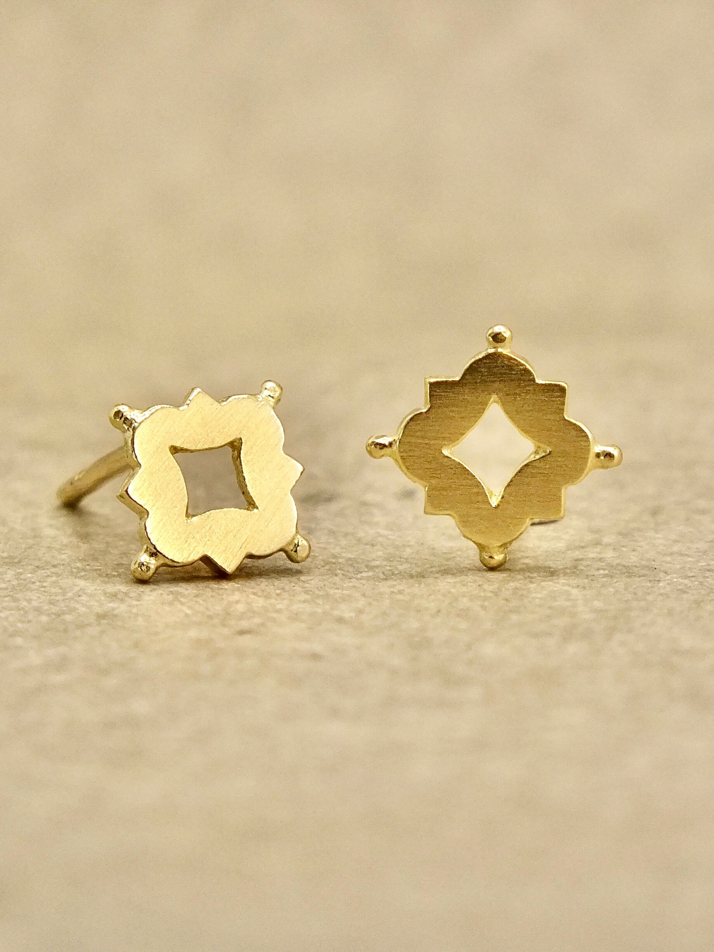 Dainty solid 18k gold stud earrings inspired by Medieval and Renaissance architecture. Featuring a quatrefoil motif with a central cutout and delicate granule accents, these minimalist studs blend historical elegance with everyday wearability.